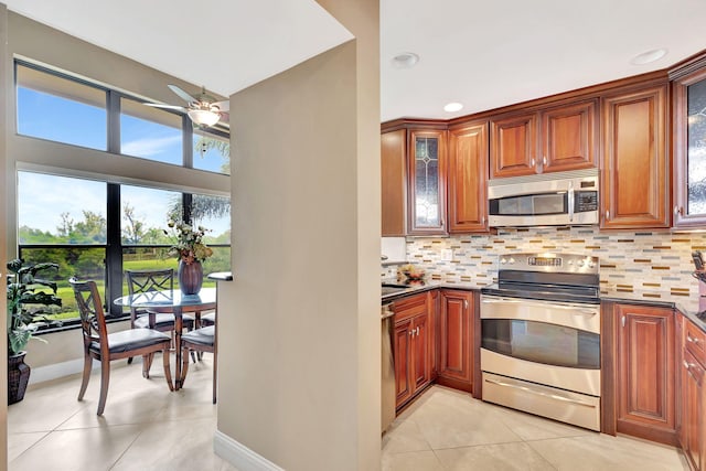 kitchen with light tile patterned floors, stainless steel appliances, tasteful backsplash, dark countertops, and glass insert cabinets