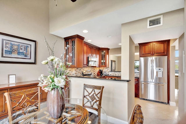 kitchen featuring visible vents, dark countertops, appliances with stainless steel finishes, glass insert cabinets, and a peninsula