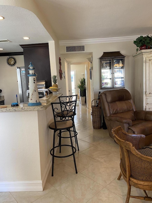 kitchen featuring crown molding, light stone counters, a textured ceiling, light tile patterned floors, and a kitchen breakfast bar