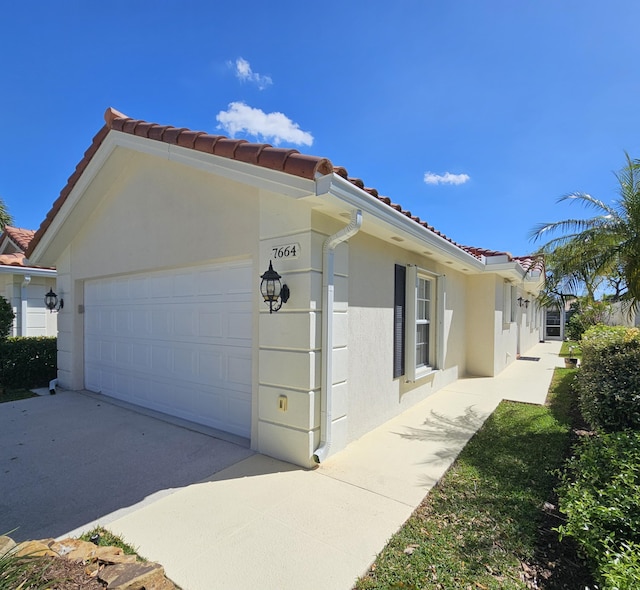 view of side of home with a garage, driveway, a tile roof, and stucco siding