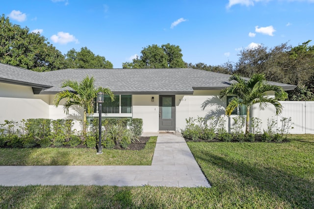 view of front facade with roof with shingles, fence, a front lawn, and stucco siding