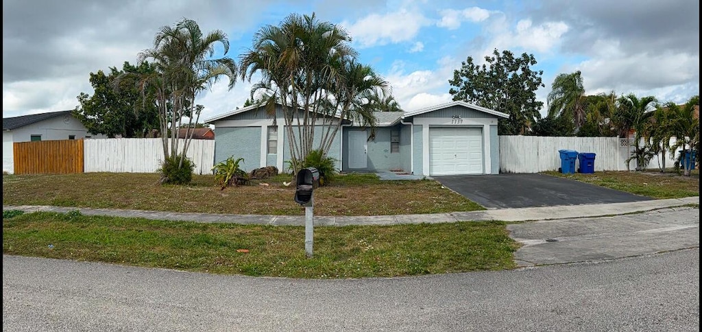 single story home with a garage, driveway, a front lawn, and fence