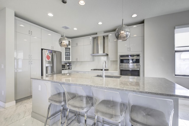 kitchen featuring appliances with stainless steel finishes, a large island, hanging light fixtures, and wall chimney range hood