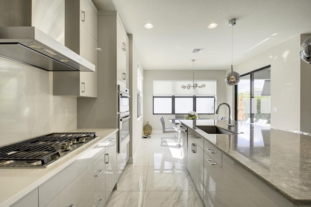 kitchen with sink, hanging light fixtures, light stone counters, stainless steel appliances, and wall chimney exhaust hood