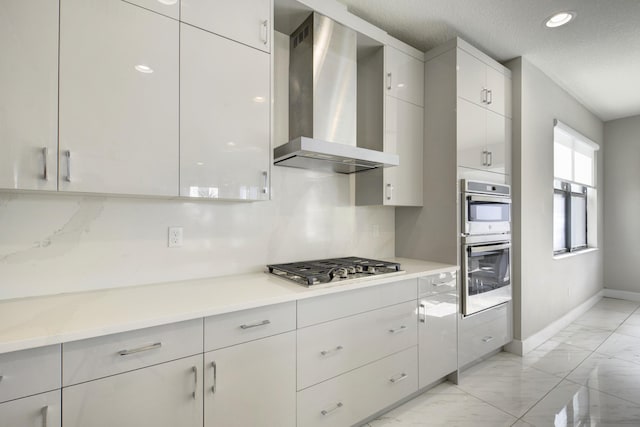 kitchen with appliances with stainless steel finishes, white cabinetry, backsplash, a textured ceiling, and wall chimney exhaust hood