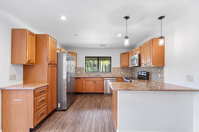 kitchen with appliances with stainless steel finishes, pendant lighting, backsplash, hardwood / wood-style floors, and kitchen peninsula