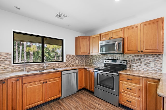 kitchen with appliances with stainless steel finishes, sink, dark hardwood / wood-style flooring, and light stone countertops