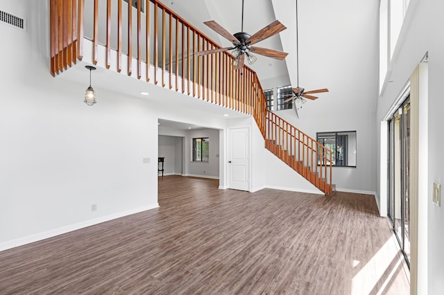 unfurnished living room featuring ceiling fan, dark hardwood / wood-style flooring, and a high ceiling