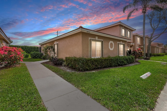 property exterior at dusk featuring a yard and stucco siding