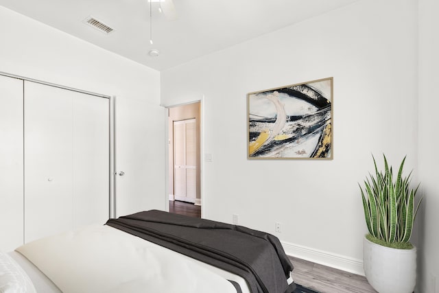 bedroom with a closet, wood finished floors, visible vents, and baseboards