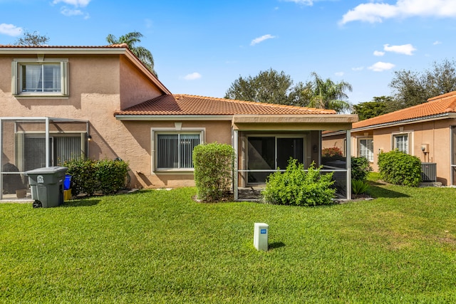 back of house with a sunroom, a yard, a tiled roof, and stucco siding