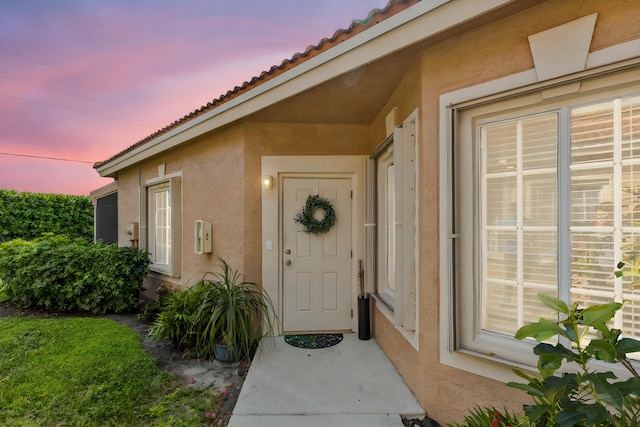 exterior entry at dusk with a tiled roof and stucco siding