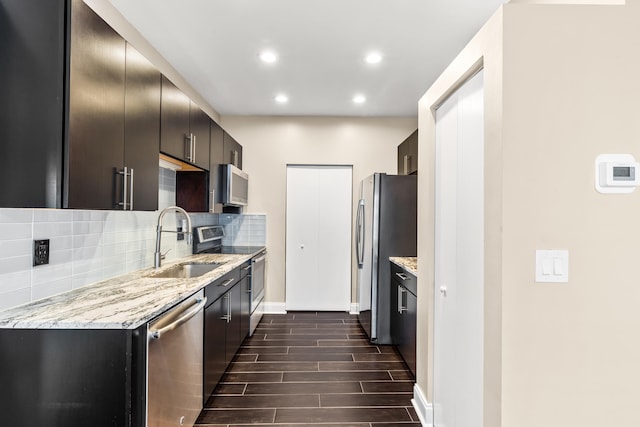 kitchen featuring light stone counters, wood finish floors, backsplash, appliances with stainless steel finishes, and a sink