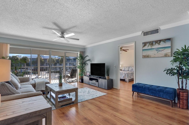 living room with light wood-type flooring, ornamental molding, a textured ceiling, and ceiling fan