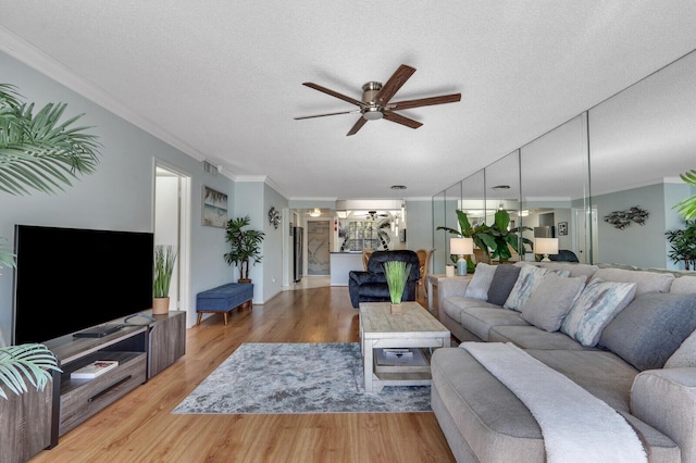 living room with ceiling fan, wood-type flooring, a textured ceiling, and ornamental molding