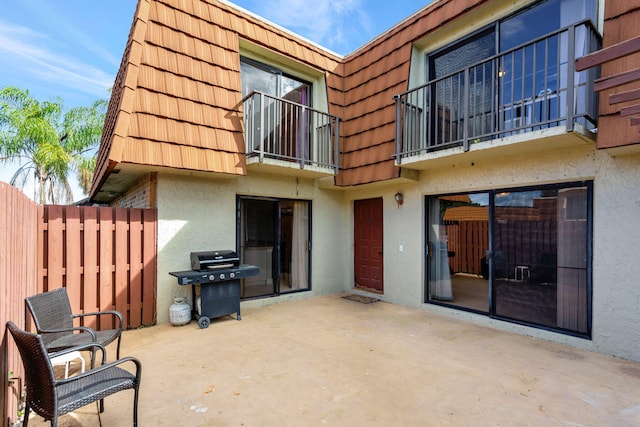 rear view of house featuring mansard roof, a patio area, fence, and stucco siding