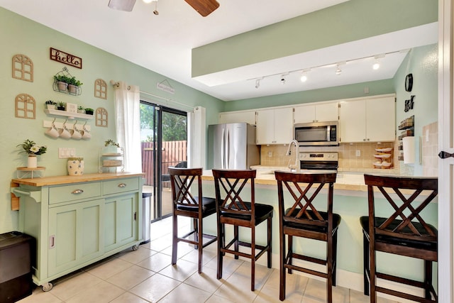 kitchen featuring a breakfast bar area, stainless steel appliances, light countertops, white cabinetry, and green cabinetry