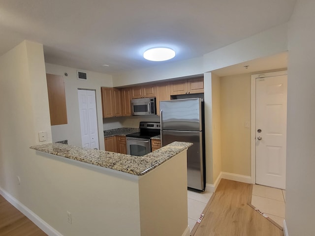 kitchen with light stone counters, stainless steel appliances, kitchen peninsula, and light hardwood / wood-style flooring