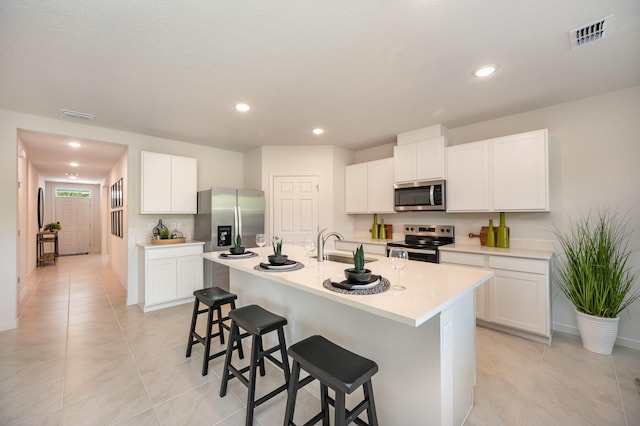 kitchen with light tile patterned floors, a kitchen breakfast bar, stainless steel appliances, white cabinets, and a kitchen island with sink