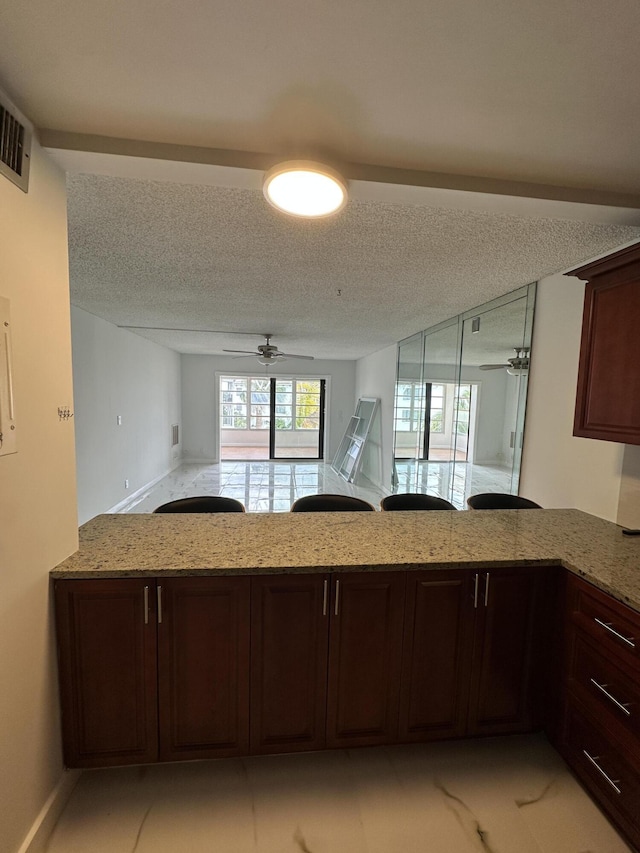 kitchen featuring ceiling fan, open floor plan, light stone counters, a peninsula, and a textured ceiling