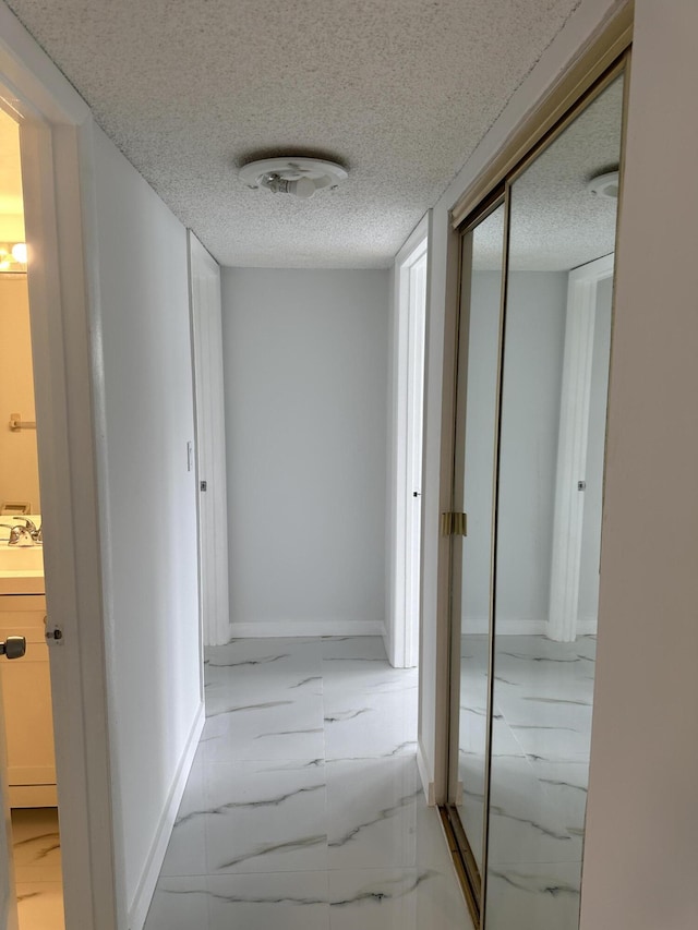 hall featuring baseboards, marble finish floor, and a textured ceiling