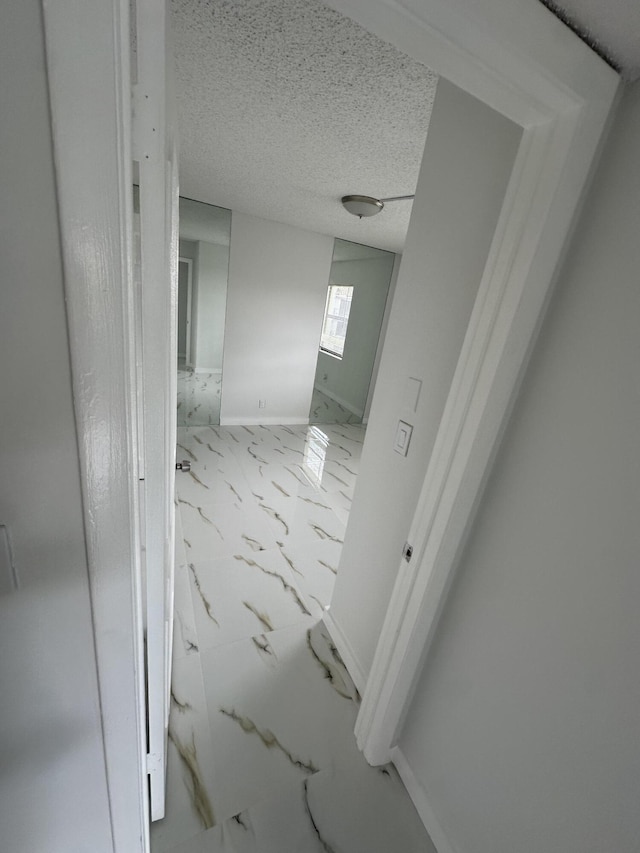 corridor featuring baseboards, marble finish floor, and a textured ceiling