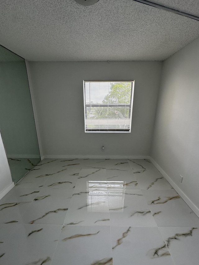 unfurnished room featuring baseboards, marble finish floor, and a textured ceiling