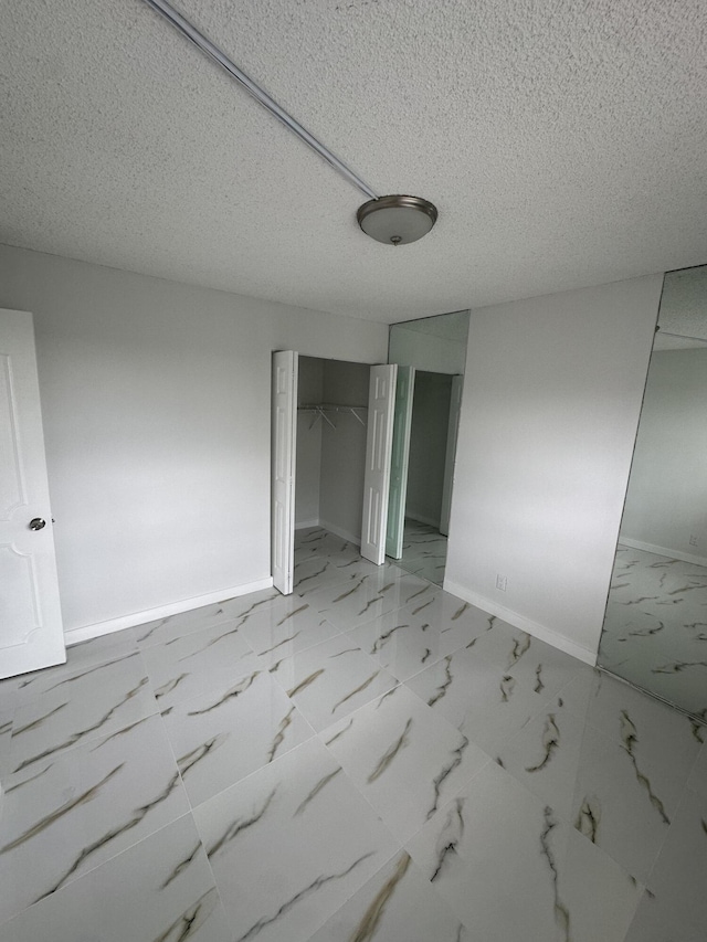 unfurnished bedroom with a closet, baseboards, a textured ceiling, and marble finish floor