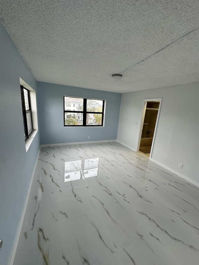 spare room with a wealth of natural light, baseboards, and marble finish floor