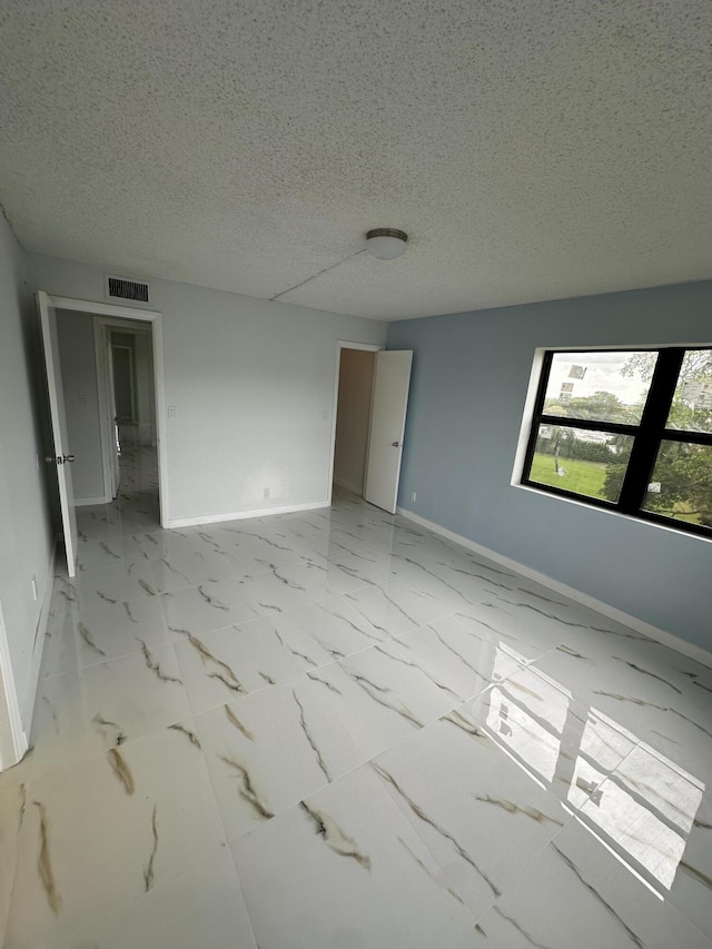 spare room with visible vents, marble finish floor, a textured ceiling, and baseboards