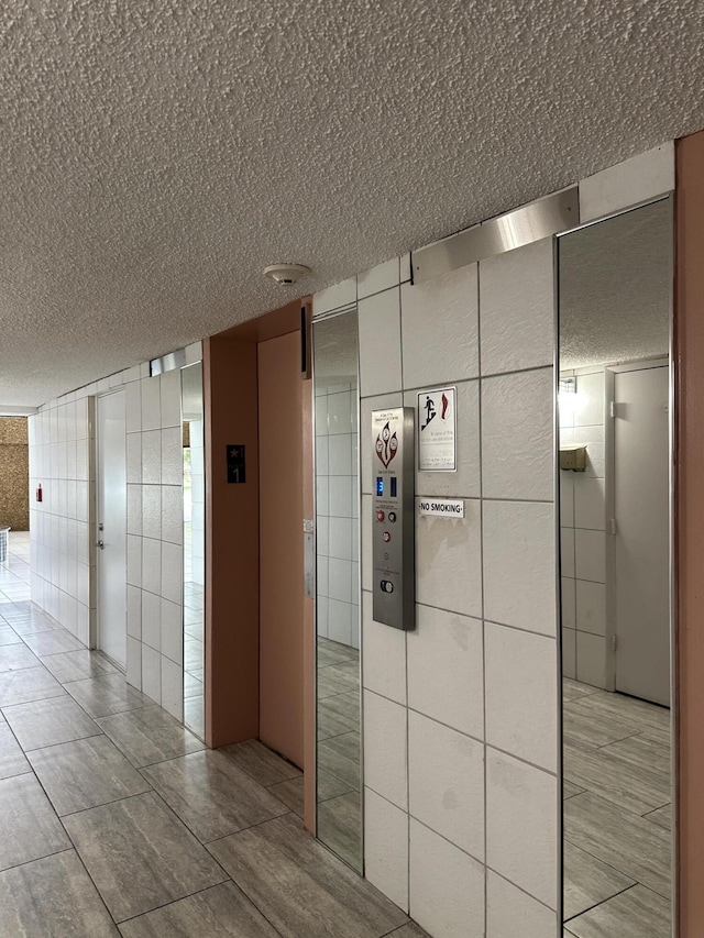 hallway with a textured ceiling and tile walls