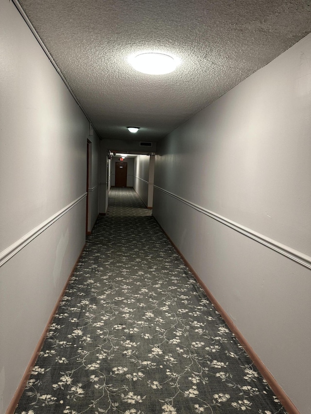 hallway with baseboards, carpet, and a textured ceiling