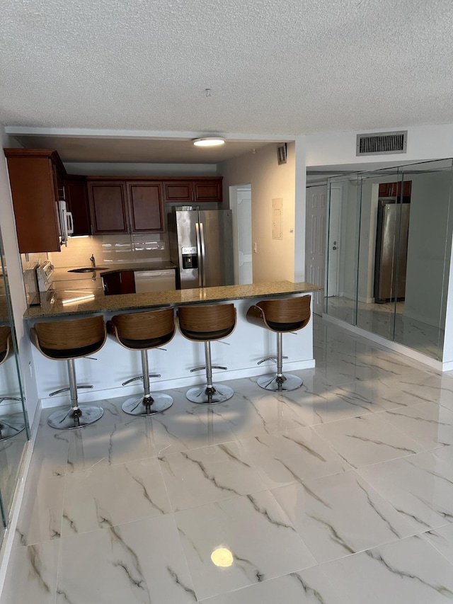 kitchen with visible vents, a kitchen bar, freestanding refrigerator, stove, and stainless steel fridge