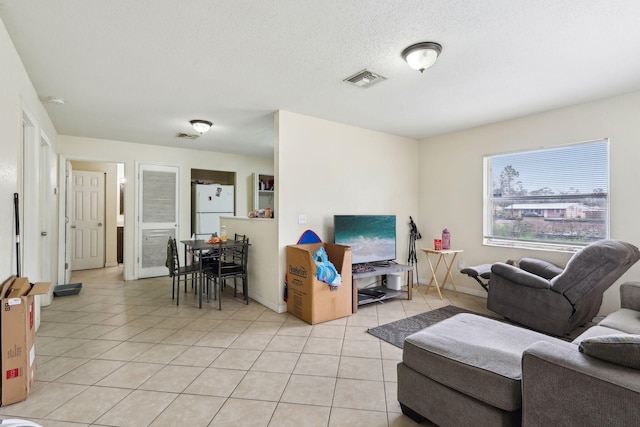 living area featuring light tile patterned floors, baseboards, visible vents, and a textured ceiling