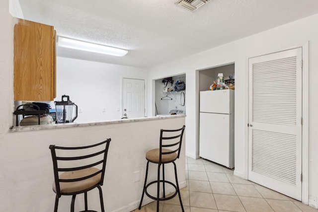 kitchen featuring a textured ceiling, light tile patterned flooring, visible vents, freestanding refrigerator, and a kitchen bar