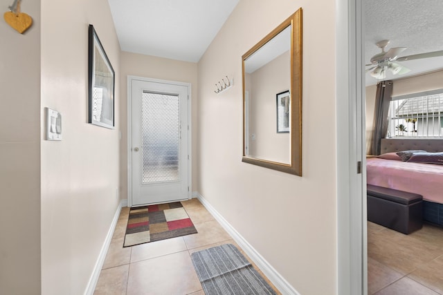 doorway featuring a ceiling fan, a textured ceiling, baseboards, and light tile patterned floors