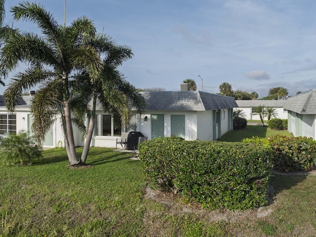 back of house with a shingled roof, a lawn, and stucco siding