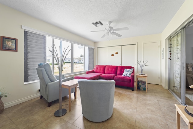 living area with light tile patterned floors, visible vents, baseboards, ceiling fan, and a textured ceiling