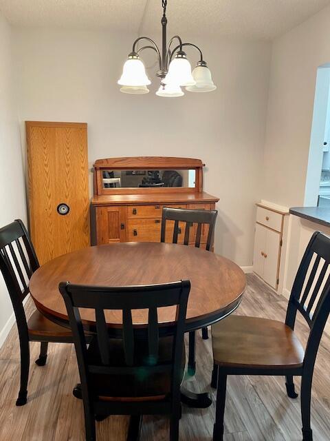 dining room with light wood-type flooring, an inviting chandelier, baseboards, and a textured ceiling