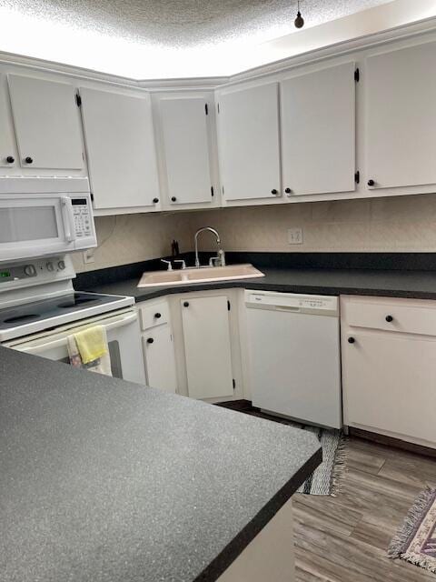 kitchen with white appliances, dark countertops, and a sink