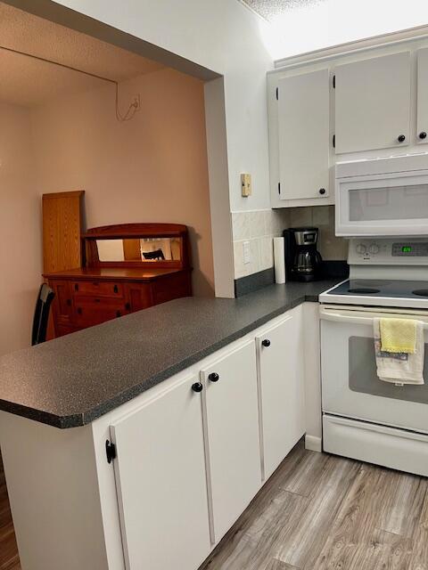 kitchen with white appliances, dark countertops, light wood-style flooring, a peninsula, and white cabinetry