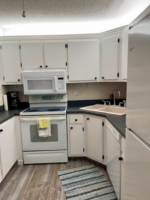 kitchen with dark countertops, white appliances, white cabinets, and a sink