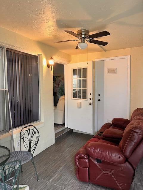 living area with a textured ceiling, dark wood-style flooring, visible vents, and a ceiling fan