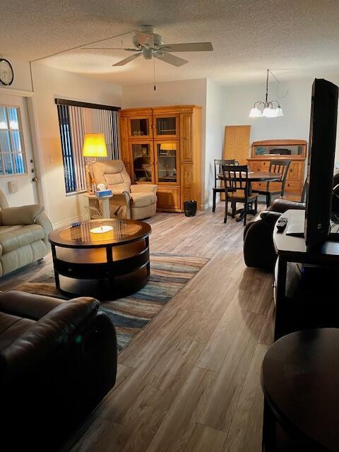 living room featuring a textured ceiling, ceiling fan with notable chandelier, and wood finished floors