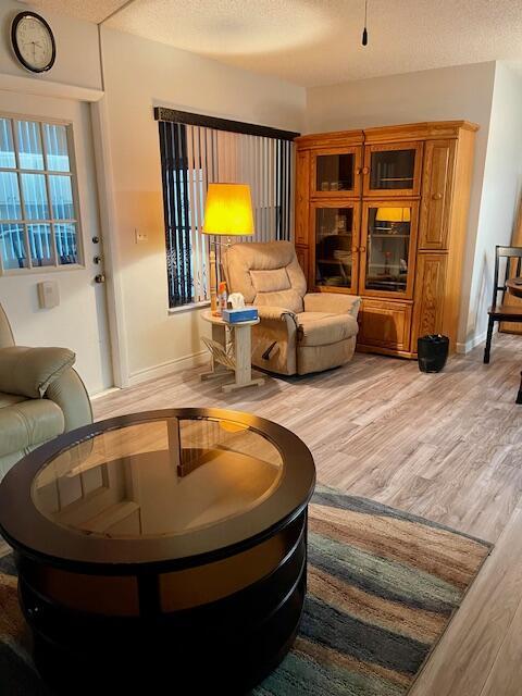 living area featuring a textured ceiling, wood finished floors, and baseboards