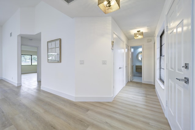 hall featuring light wood-type flooring, visible vents, and baseboards