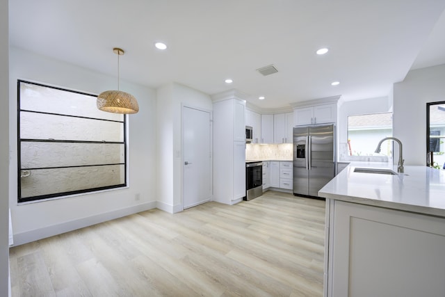 kitchen featuring decorative backsplash, stainless steel appliances, white cabinetry, pendant lighting, and a sink