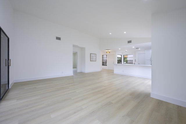 unfurnished living room featuring high vaulted ceiling, light wood-style flooring, visible vents, and baseboards