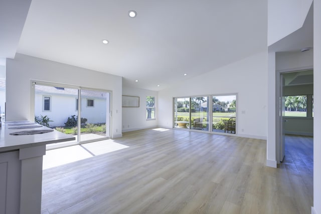 unfurnished living room with lofted ceiling, light wood finished floors, baseboards, and recessed lighting