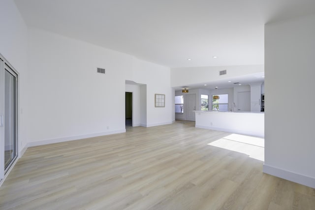 unfurnished living room with high vaulted ceiling, a sink, visible vents, baseboards, and light wood-style floors